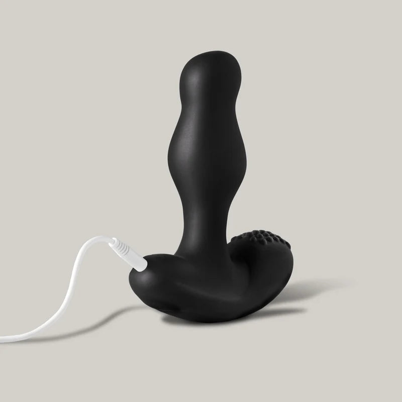 giddi thor rotating prostate massager plugged into white usb charging cord on a neutral background