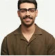 Person with glasses wearing a brown shirt in a neutral pose against a plain background.