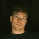 Person with short hair looking at the camera against a dark background.
